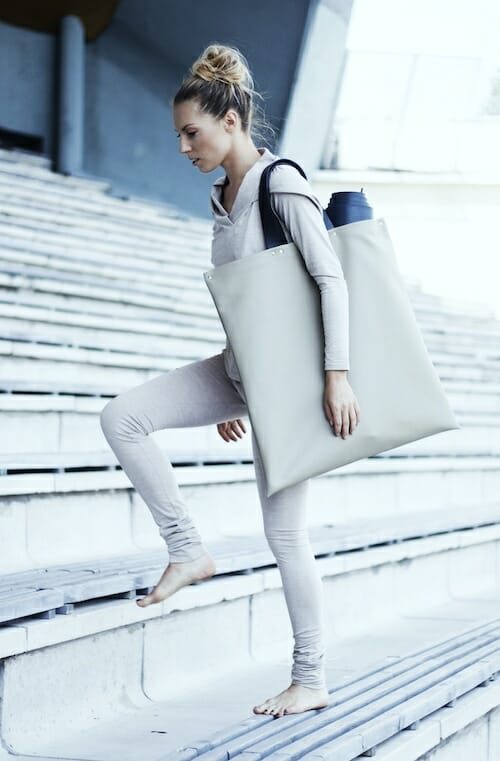Woman in light grey yoga suit with a large tote bag walking up stadium steps
