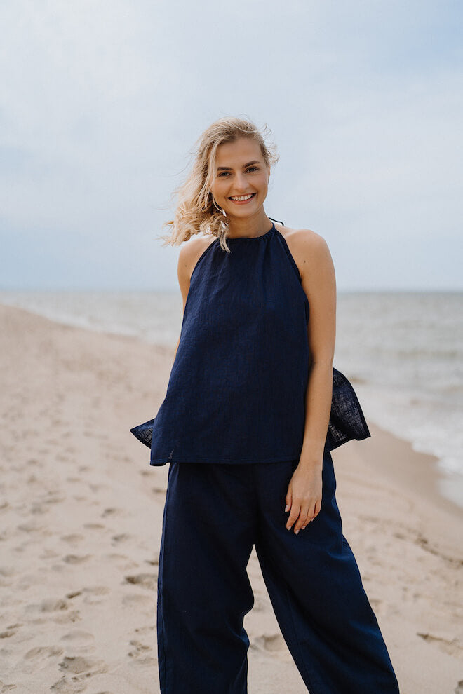 Smilende kvinde i marineblå hør-top med halterneck og bukser på en strand