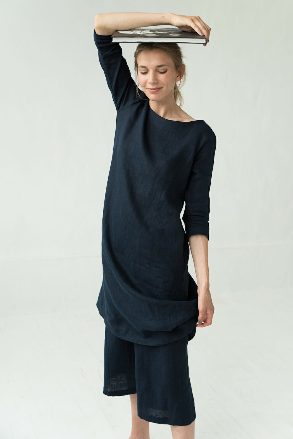 Woman in a dark blue linen dress with sleeves balancing books on her head
