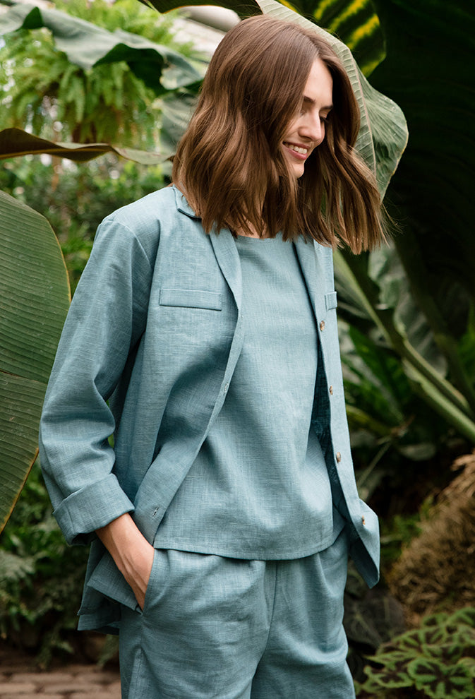Woman in a sage green linen jacket, top and trousers among tropical plants