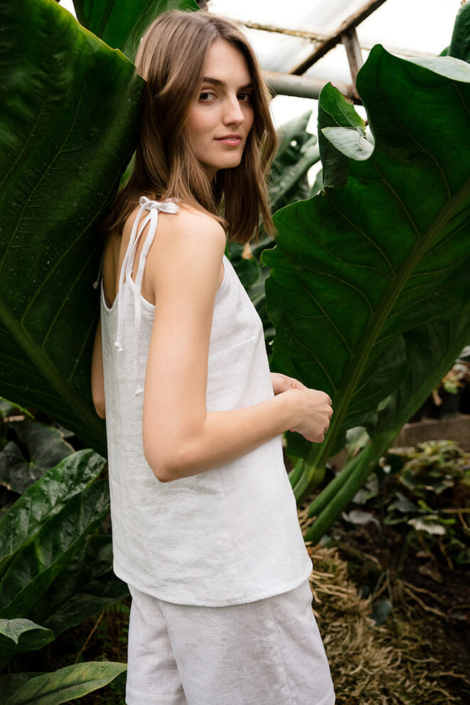 Woman in a white linen top and trousers among large green leaves