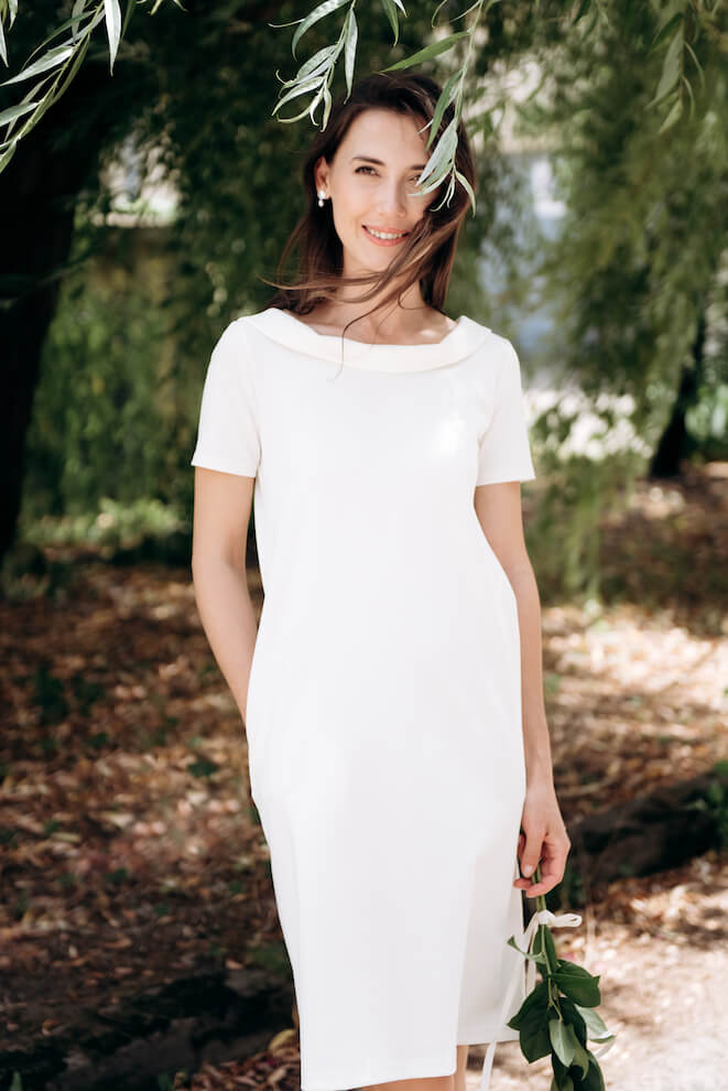 Frau in weißem kurzärmeligem Midikleid im Freien zwischen Bäumen