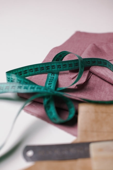 Pink linen fabric with a green tape measure and tailor's tools
