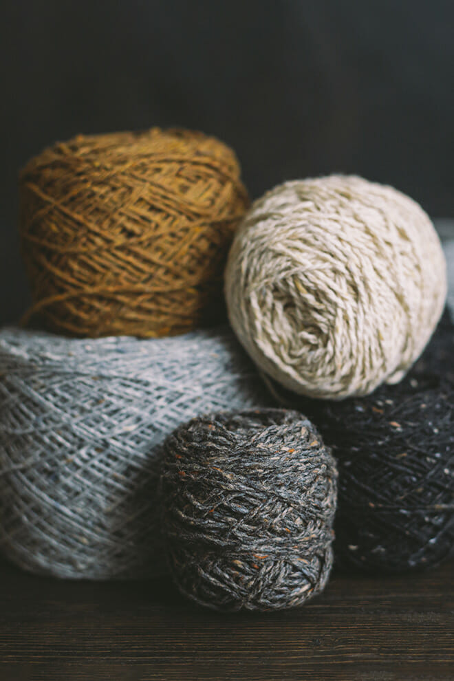 Balls of wool yarn in ochre, cream and grey on a dark background