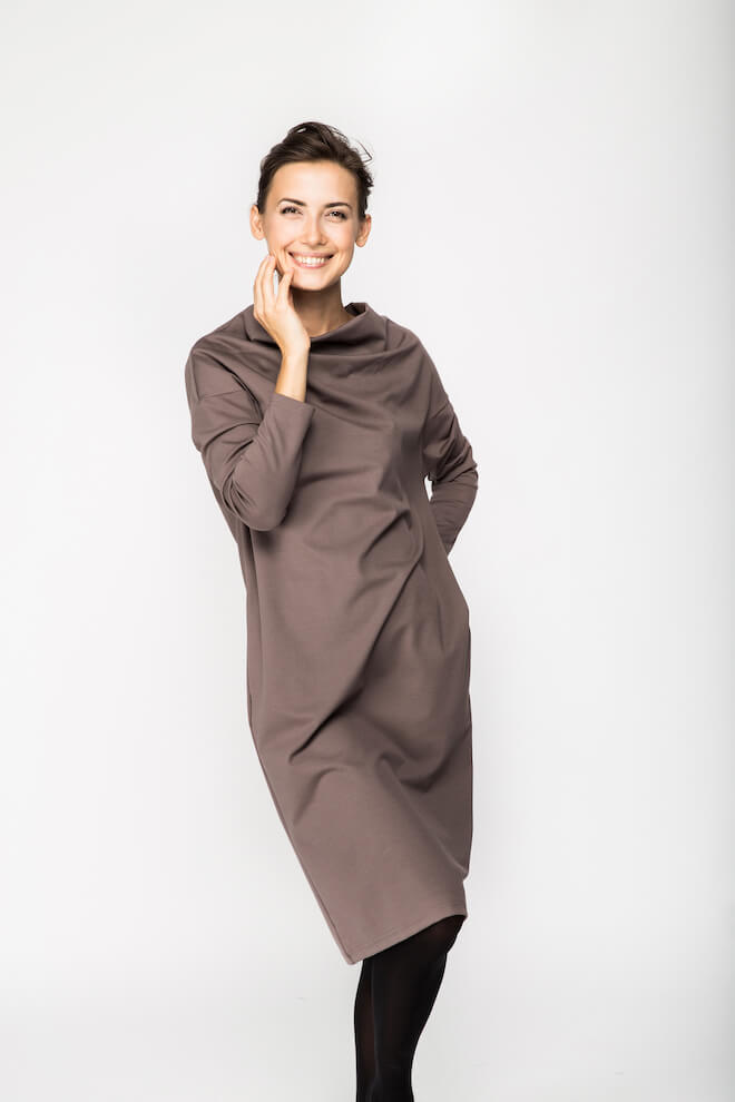 Smiling woman in a taupe long-sleeve knee-length dress with a high neck