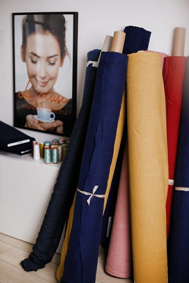 Rolls of linen fabric in navy, ochre and pink leaning against a studio wall