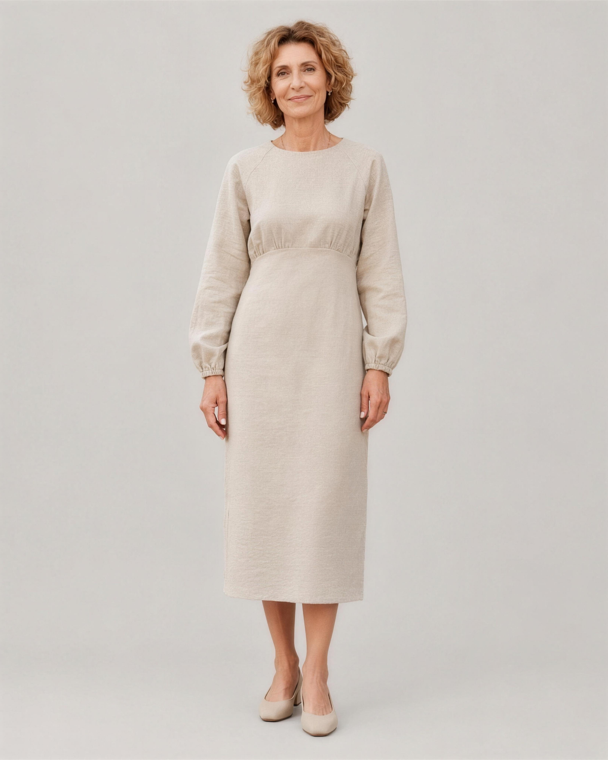 A woman standing in a studio, facing camera, full length, wearing a light beige long-sleeve linen midi dress with a gathered waist and elastic cuffs. #Color_Beige