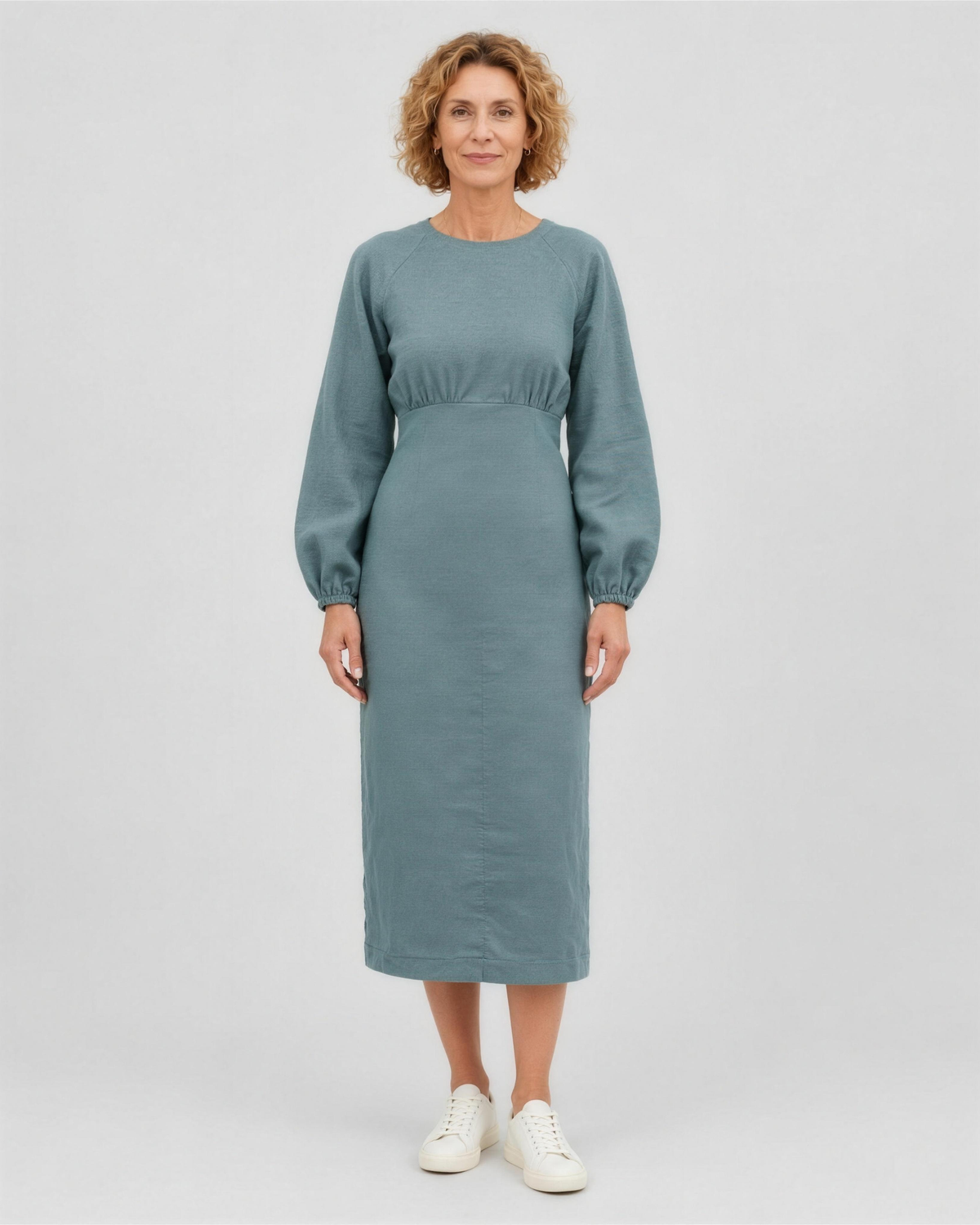 A woman standing in a studio, facing camera, full length, wearing a muted dusty blue-green teal linen midi dress with a gathered waist and elastic cuffs. #Color_Teal