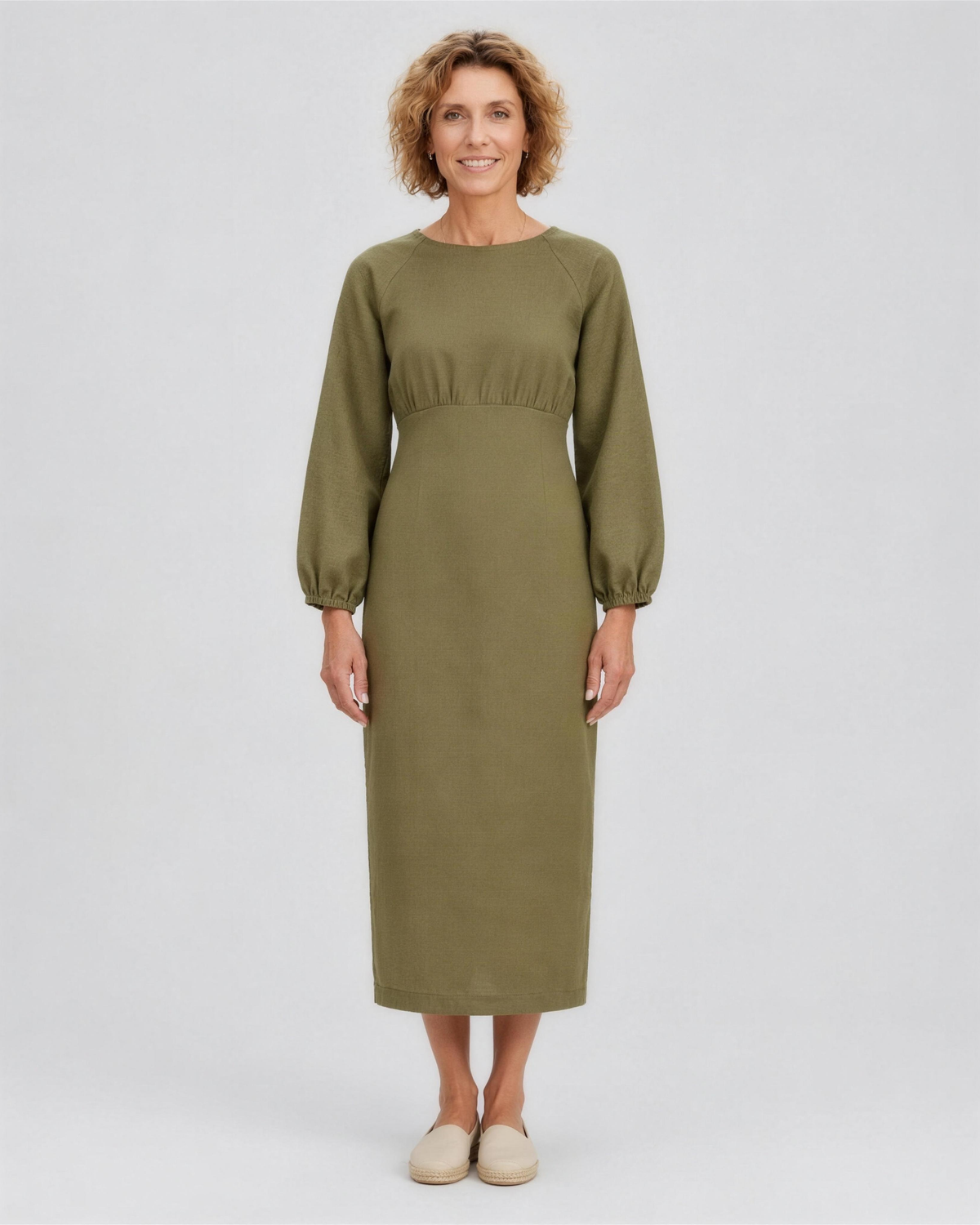 A woman standing in a studio, facing camera, full length, wearing an olive green linen midi dress with a gathered waist and elastic cuffs. #Color_Olive green