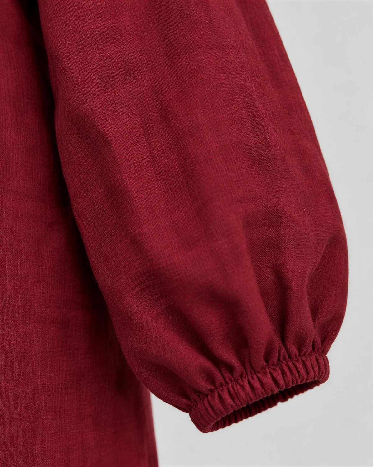 Close-up of deep burgundy linen fabric texture and sleeve cuff detail on a midi dress. #Color_Burgundy