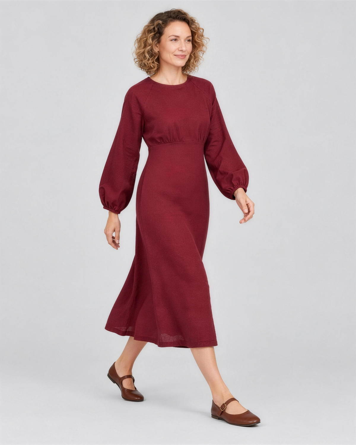 A woman walking, side view, wearing a deep burgundy linen midi dress, showing how the linen fabric moves. #Color_Burgundy