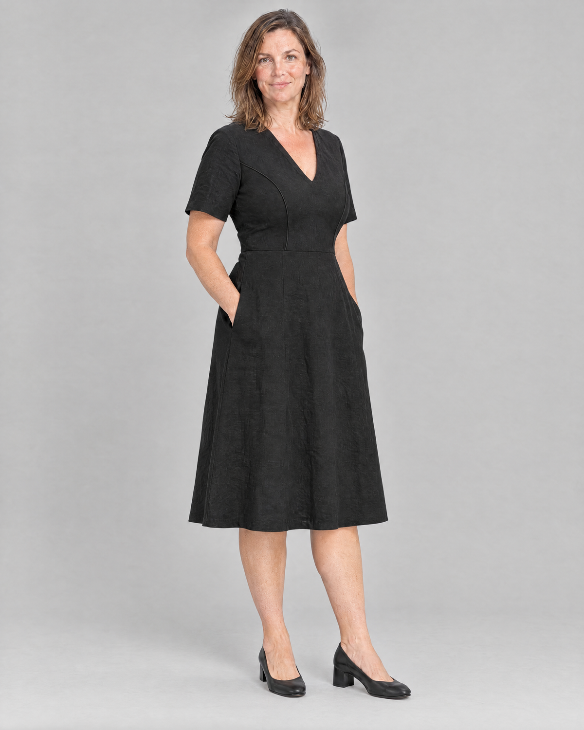 ROOM black linen V-neck A-line midi dress, three-quarter view with hands in the side pockets