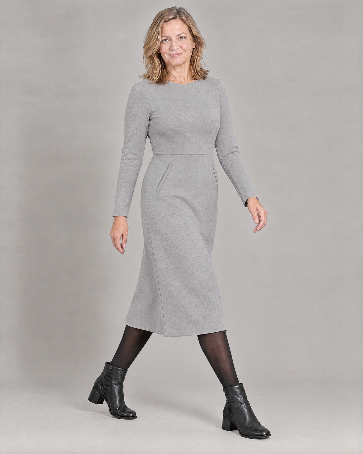 Woman taking a full stride in the GLIDE light grey wool midi dress with black tights and boots