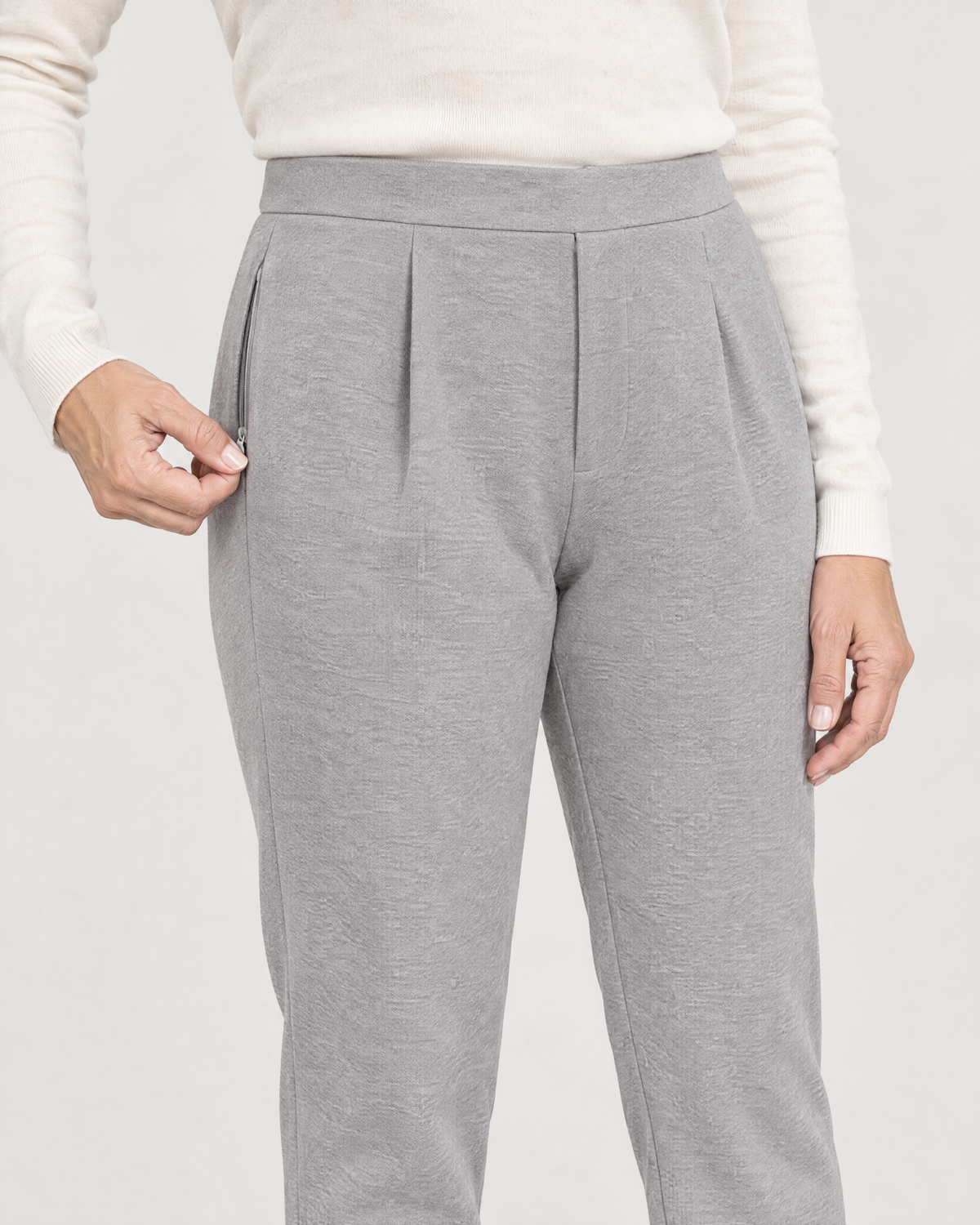 Close-up of the concealed zipped side-seam pocket on light grey wool knit trousers