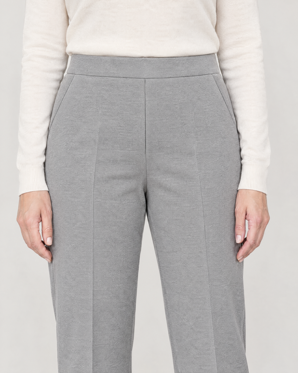 Close-up of the flat 4 cm waistband, slanted pocket and pressed crease on light grey wool knit trousers