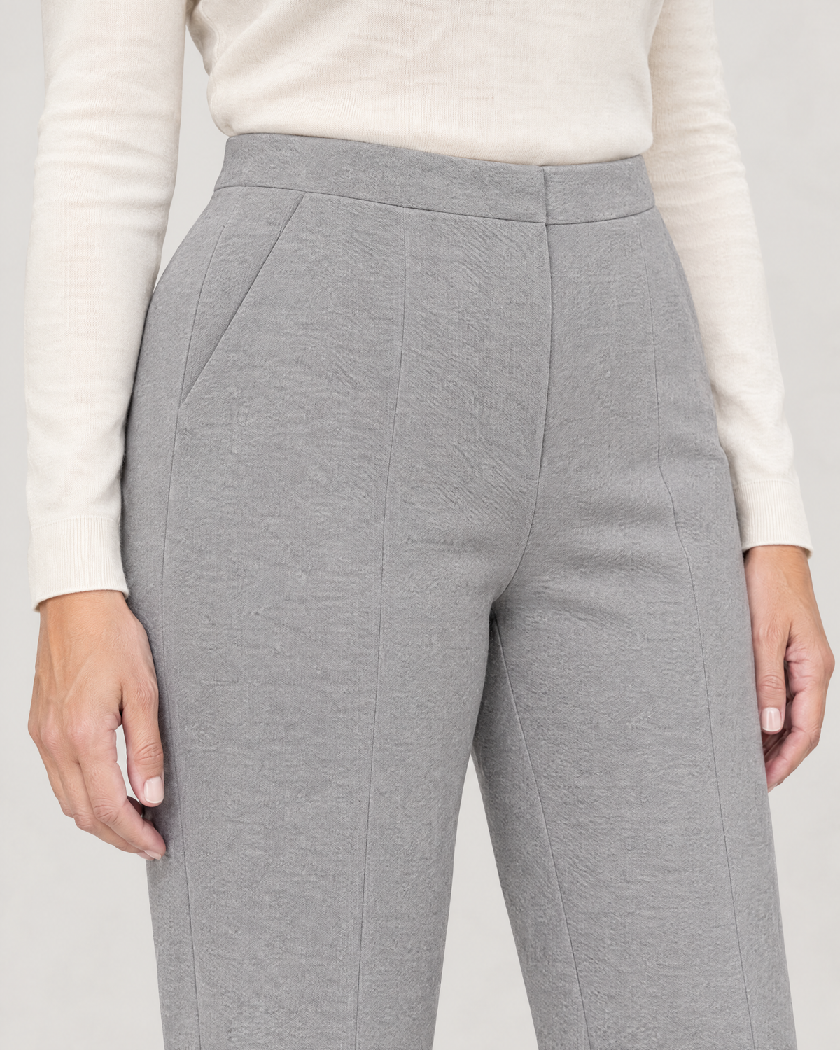 Close-up of the contoured waistband, concealed zip, slanted pocket and pressed crease in light grey wool knit