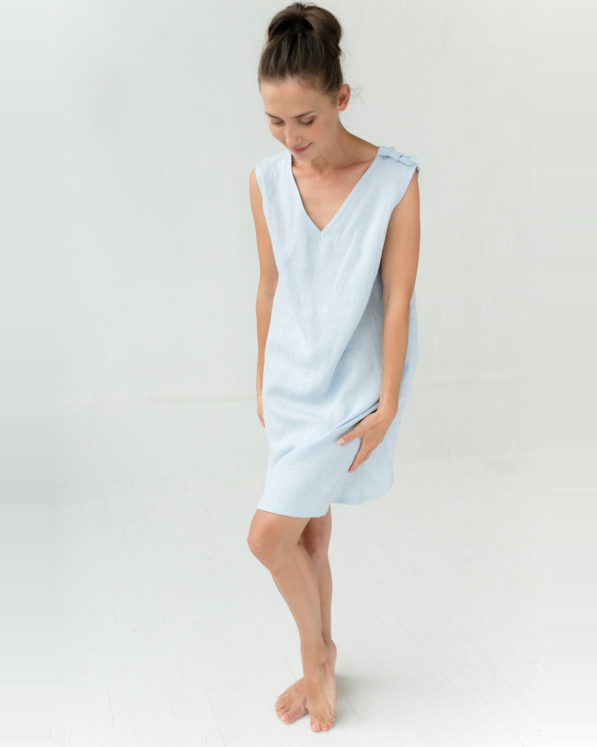 A woman in a light blue linen night dress with a wide plunging V neckline and a small bow on the shoulder.