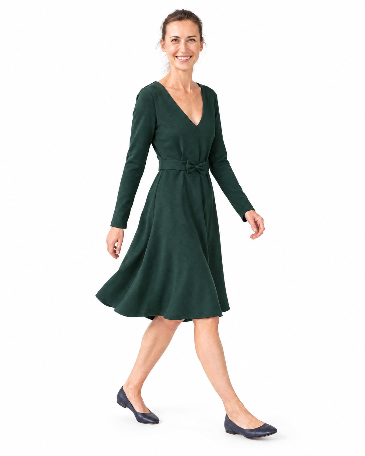 A woman walking in a dark green long-sleeve Punto Milano dress, side view showing the A-line skirt in motion. #Color_Green