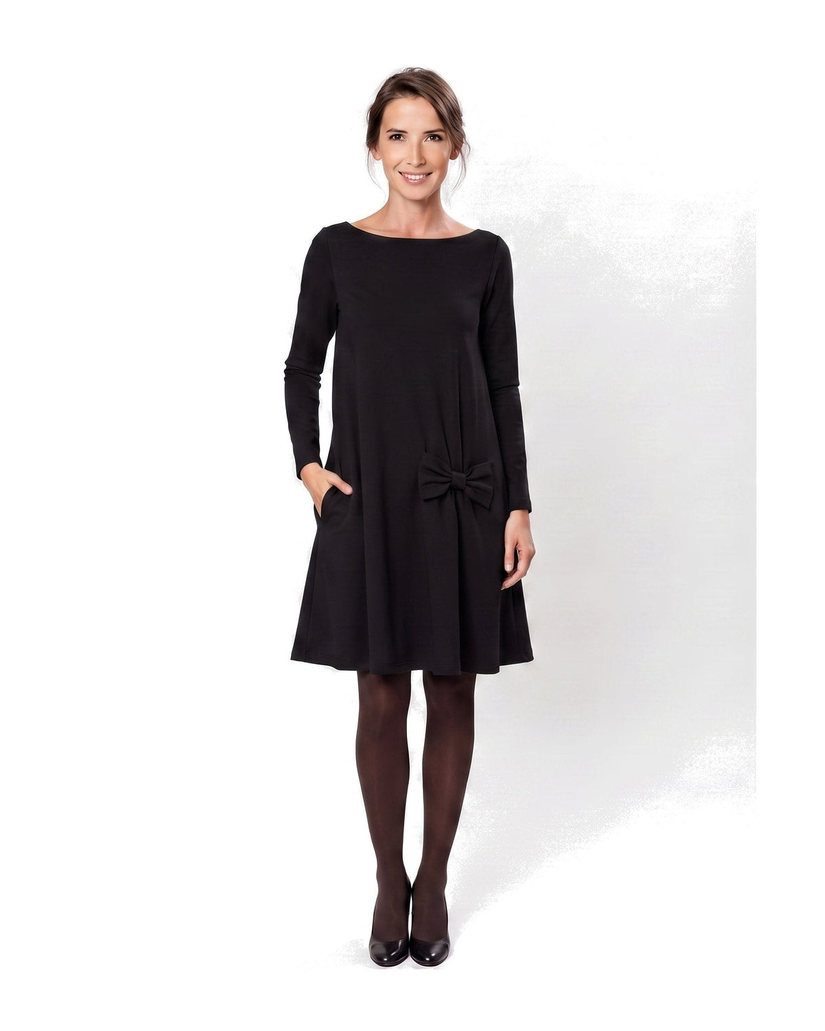 A woman modeling a black long-sleeve A-line dress with a boat neckline, side pockets, and a bow detail at the waist. #Color_Black