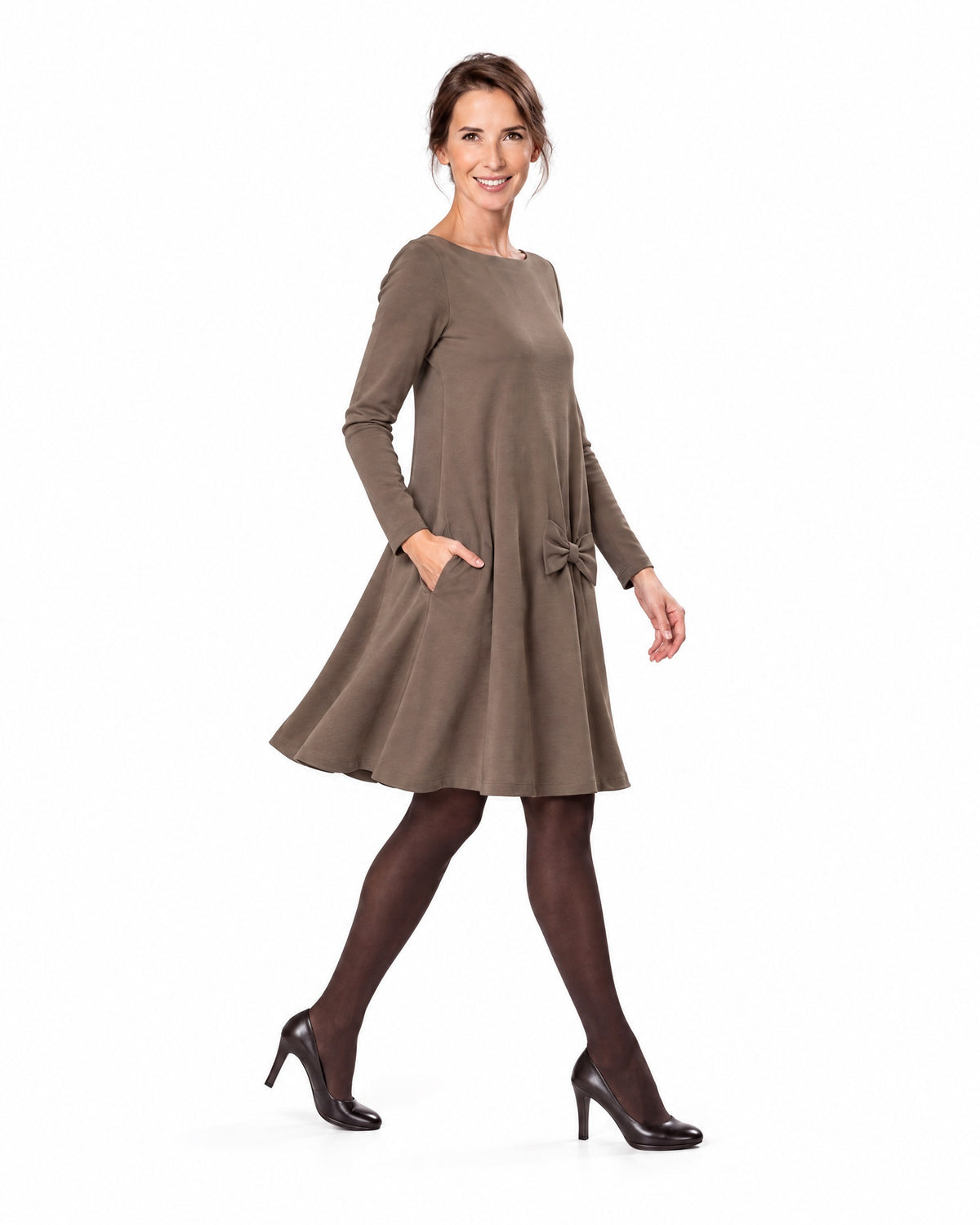 A woman modeling a brown long-sleeve A-line dress with a boat neckline and bow-detail pocket, shown in profile while walking. #Color_Brown