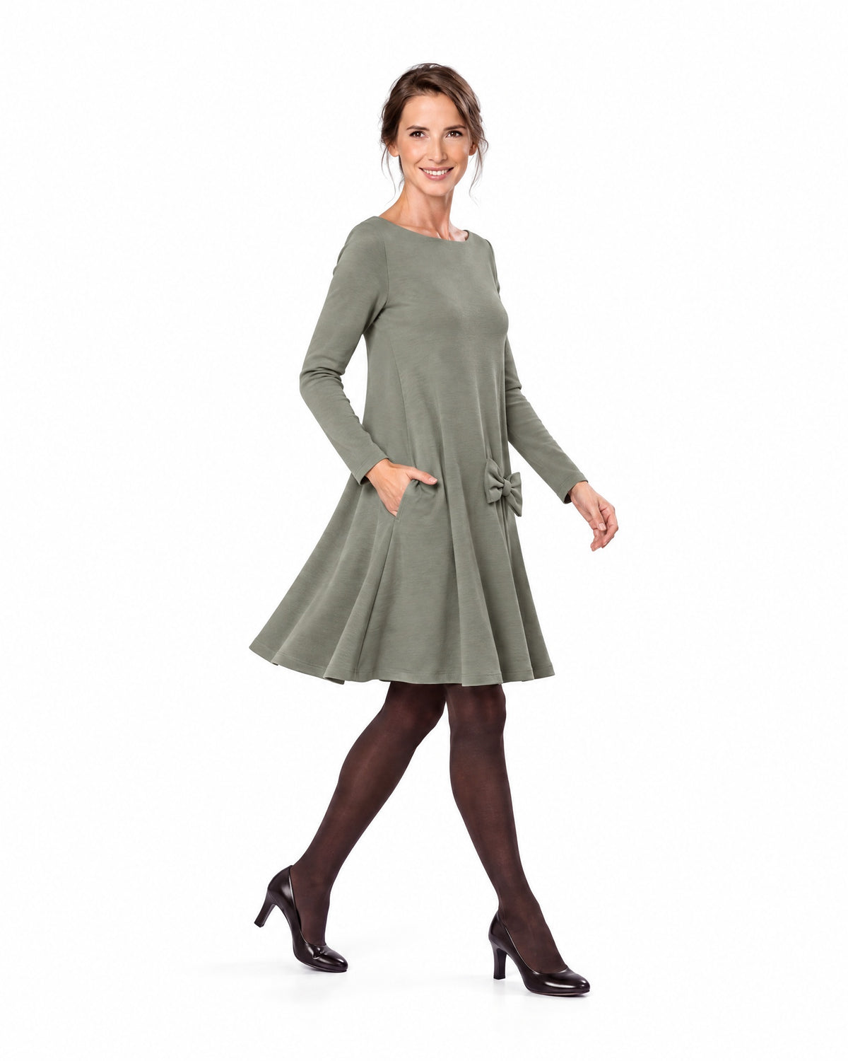 A woman modeling a gray-green long-sleeve A-line dress with a boat neckline and bow-detail pocket, shown in profile while walking. #Color_Gray green
