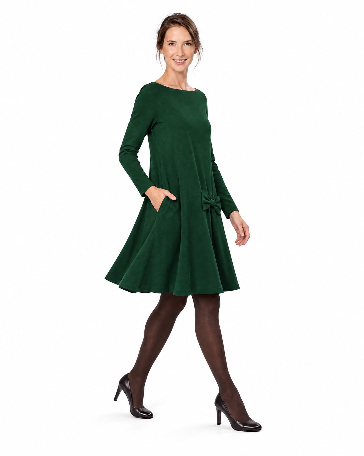 A woman modeling a dark green long-sleeve A-line dress with a boat neckline and bow-detail pocket, shown in profile while walking. #Color_Green