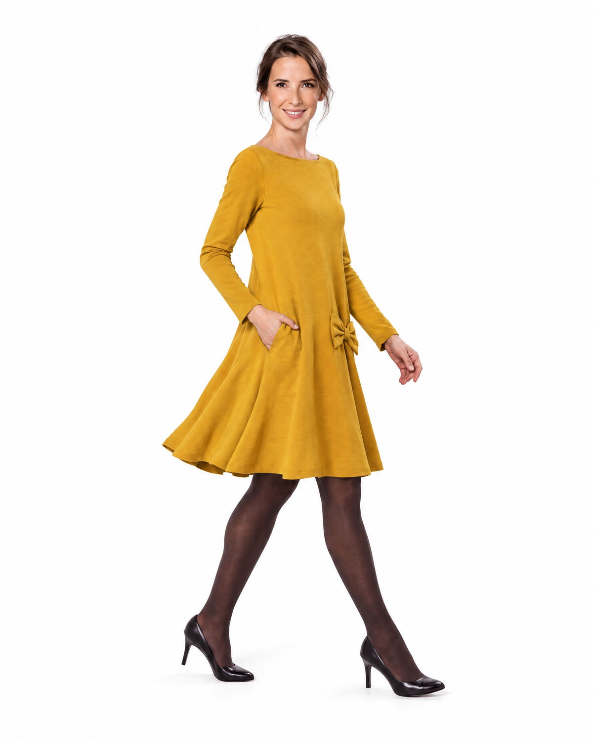 A woman modeling a mustard yellow long-sleeve A-line dress with a boat neckline and bow-detail pocket, shown in profile while walking. #Color_Yellow