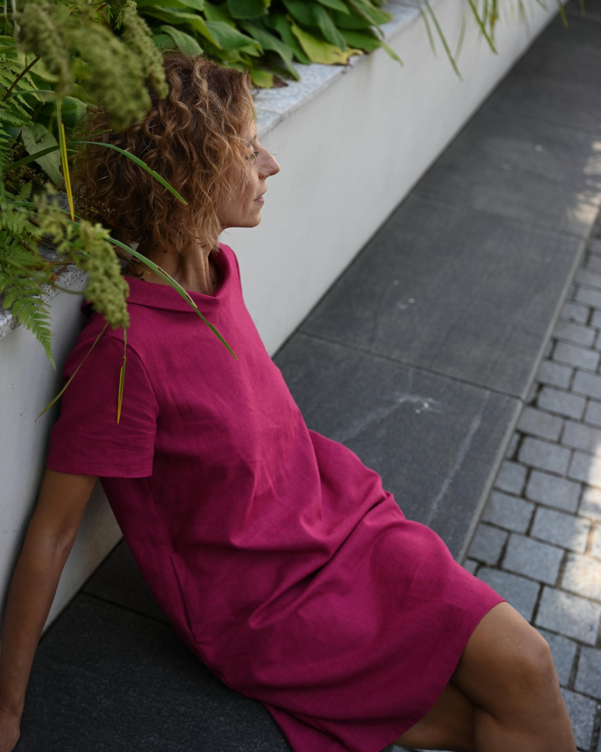 LeMuse STORY linen dress in cerise – seated on stone steps #Color_Cerise
