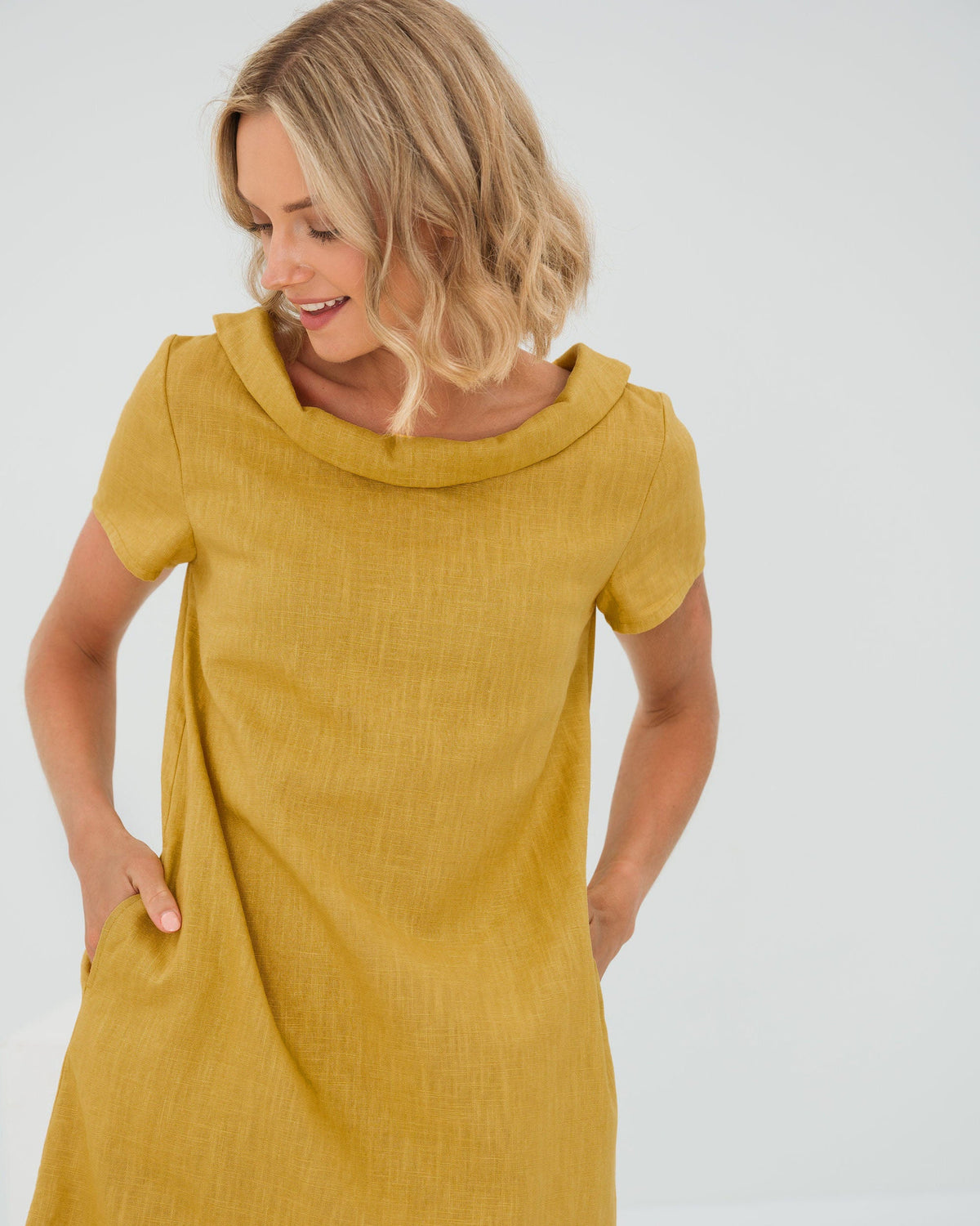 LeMuse STORY linen dress in ochre – studio front view, hands in pockets, looking down #Color_Ochre