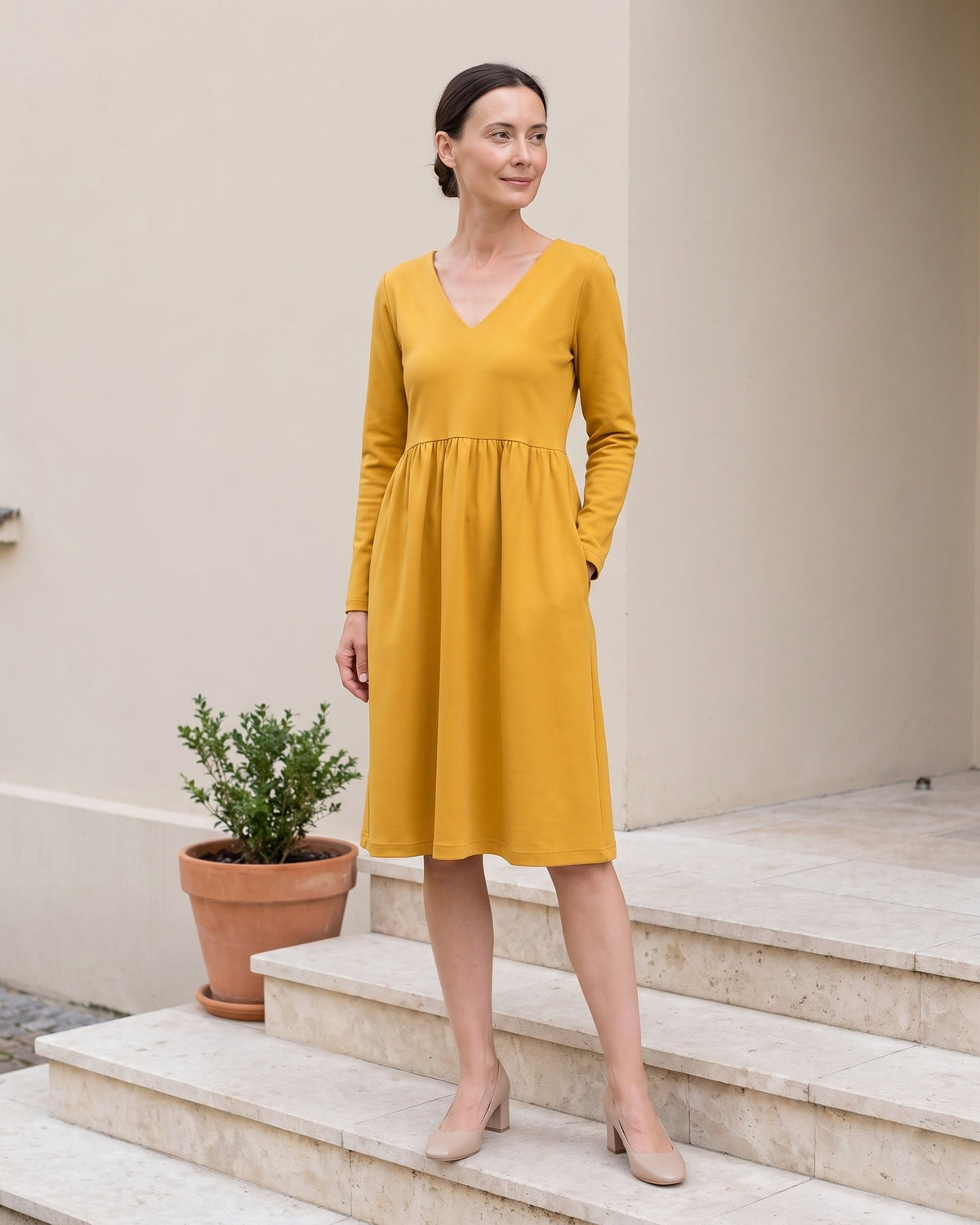 Woman wearing SUNSHINE Punto Milano midi dress in yellow, lifestyle photo on stone steps with potted plant #Color_Yellow