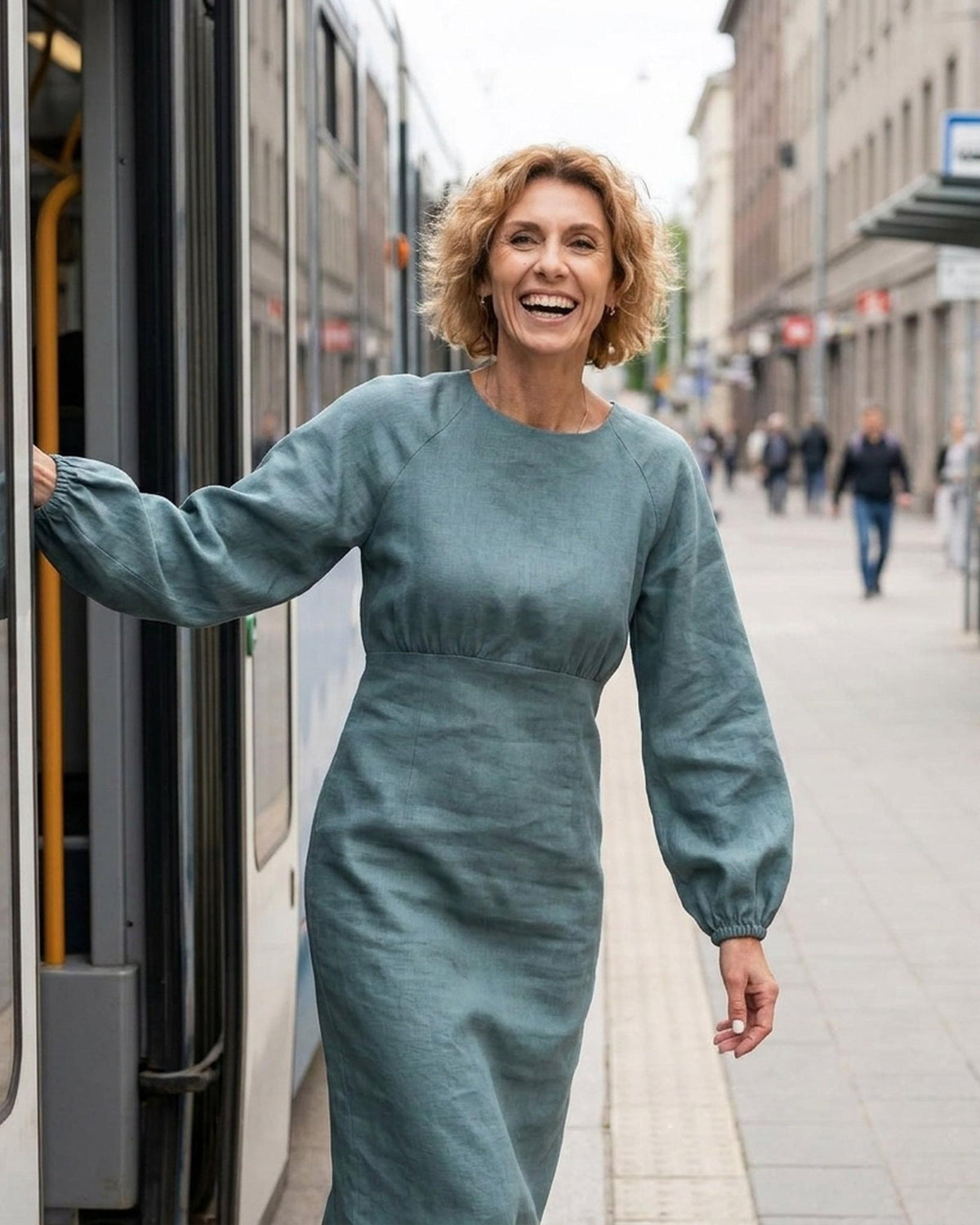 A woman boarding a tram, smiling, wearing a long-sleeve teal linen midi dress with a gathered waist, full length front view. #Color_Teal
