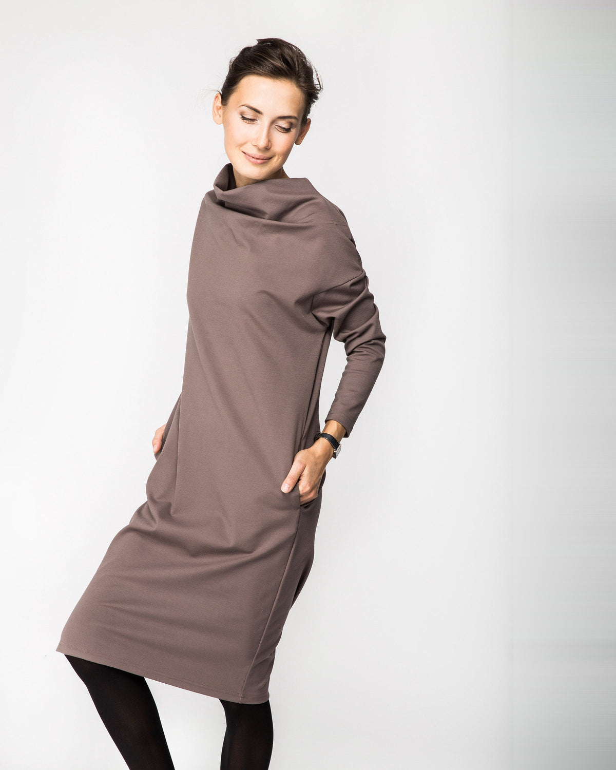 A woman wearing a taupe brown long-sleeve cowl-neck midi dress with side pockets, three-quarter front view showing the cowl neckline. #Color_Cacao