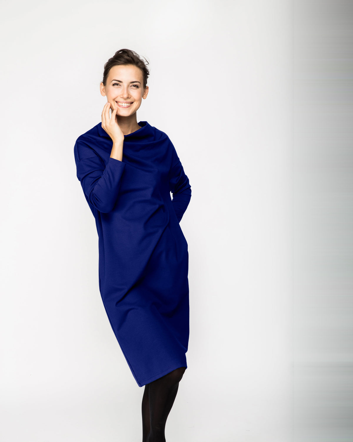 A woman wearing a bright royal blue long-sleeve cowl-neck midi dress with side pockets, standing against a white background, front view. #Color_Sapphire blue