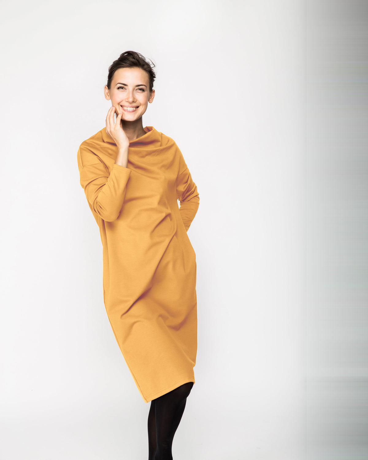 A woman wearing a mustard yellow long-sleeve cowl-neck midi dress with side pockets, standing against a white background, front view. #Color_Yellow