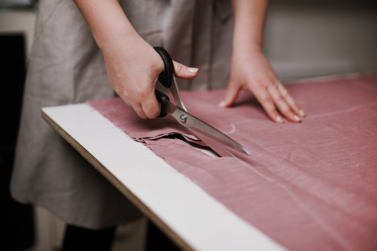 Hands cutting pink linen fabric with tailor's scissors