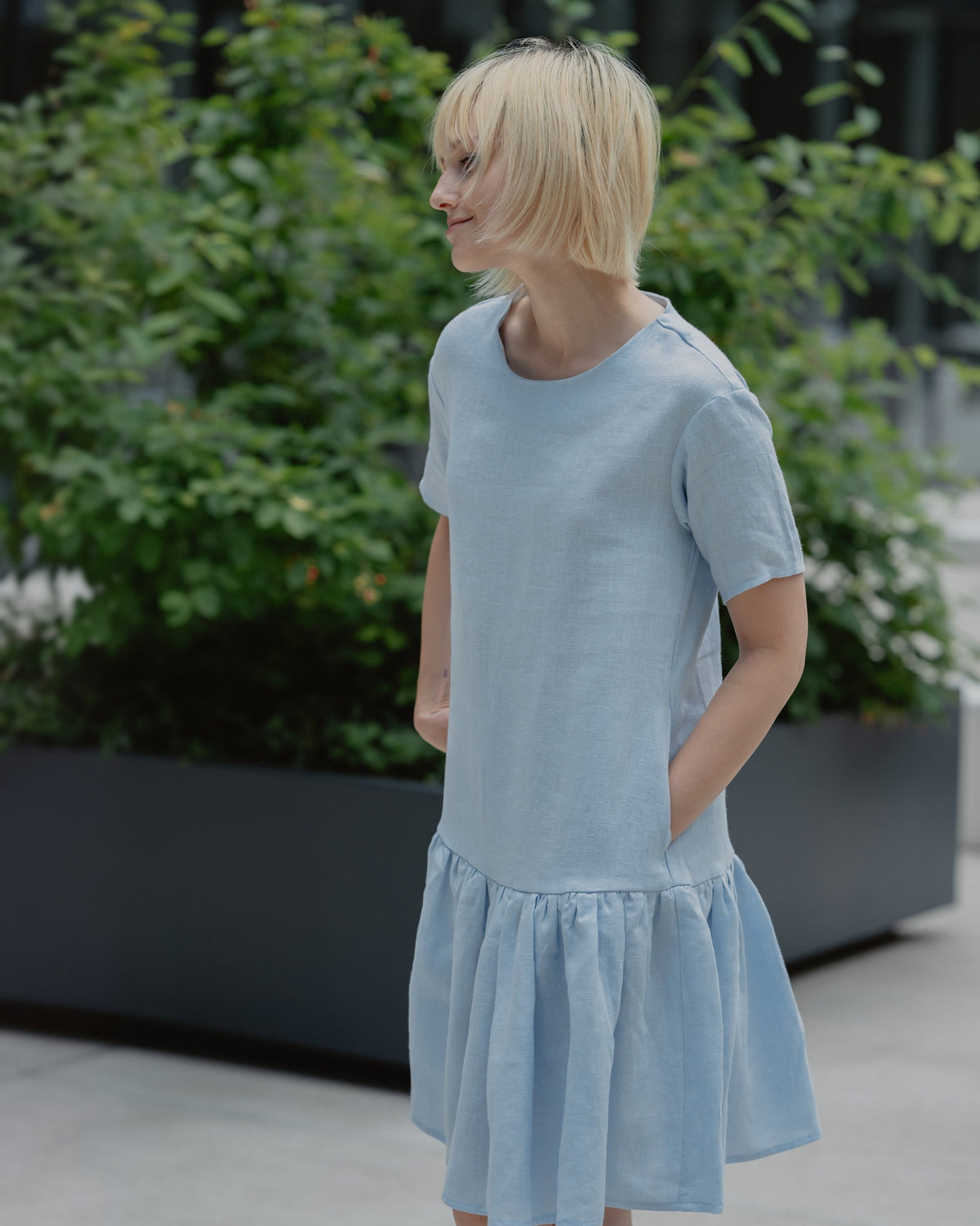 LeMuse BLOSSOM linen dress in light blue – 3/4 view outdoors, looking aside, hand in pocket #Color_Light blue