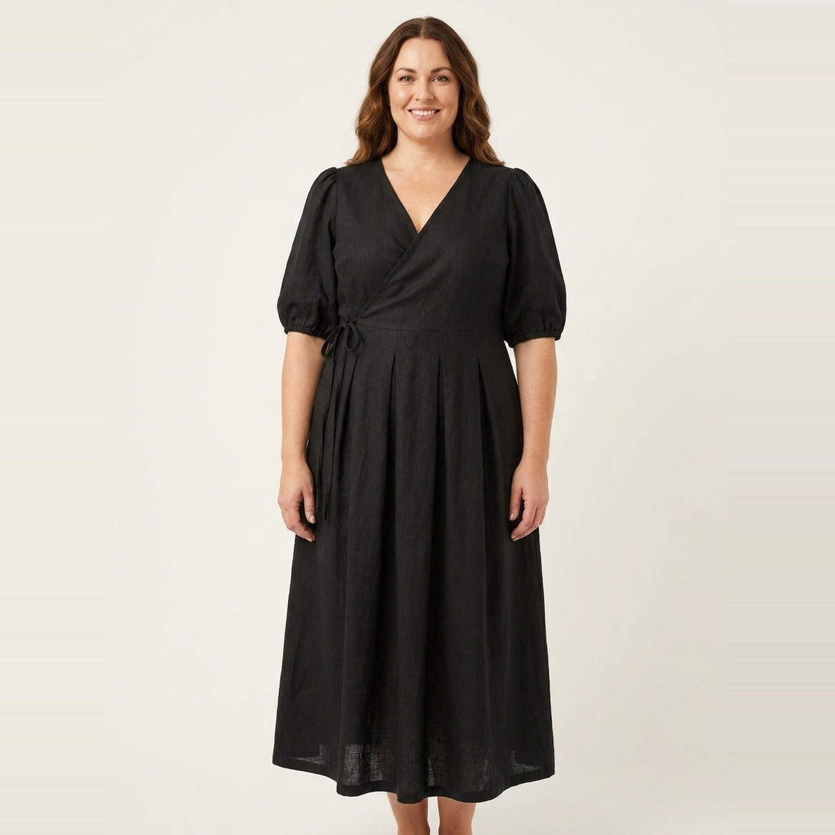 A woman standing facing forward, full length, wearing a black midi wrap dress with short puff sleeves and a V-neckline, photographed against a plain light studio background. #Color_Black