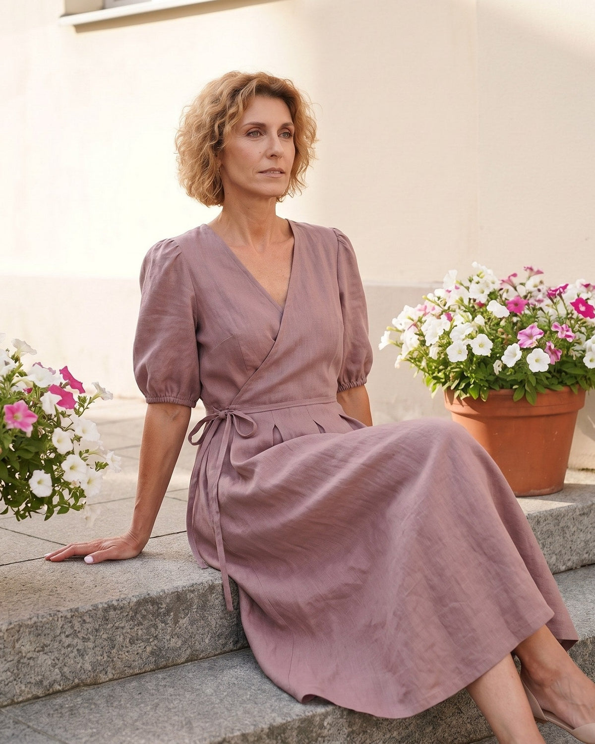 BONNIE – Linen Blend Puff Sleeve Tie-Waist Midi Dress – Dusty rose suknelė, lifestyle photo, seated outdoors among potted flowers #Color_Dusty rose