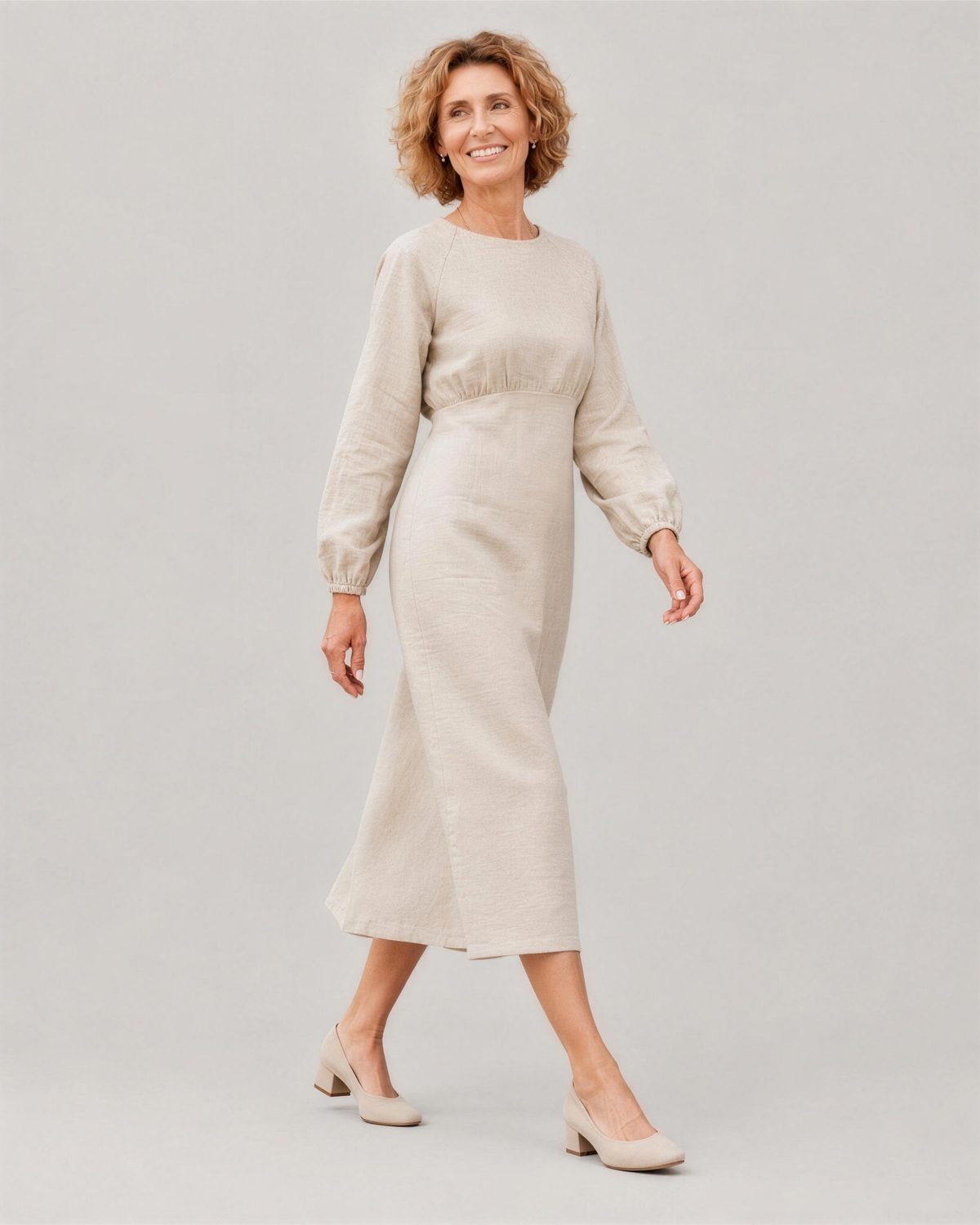 A woman walking, side view, wearing a light beige long-sleeve linen midi dress, showing how the linen fabric moves. #Color_Beige