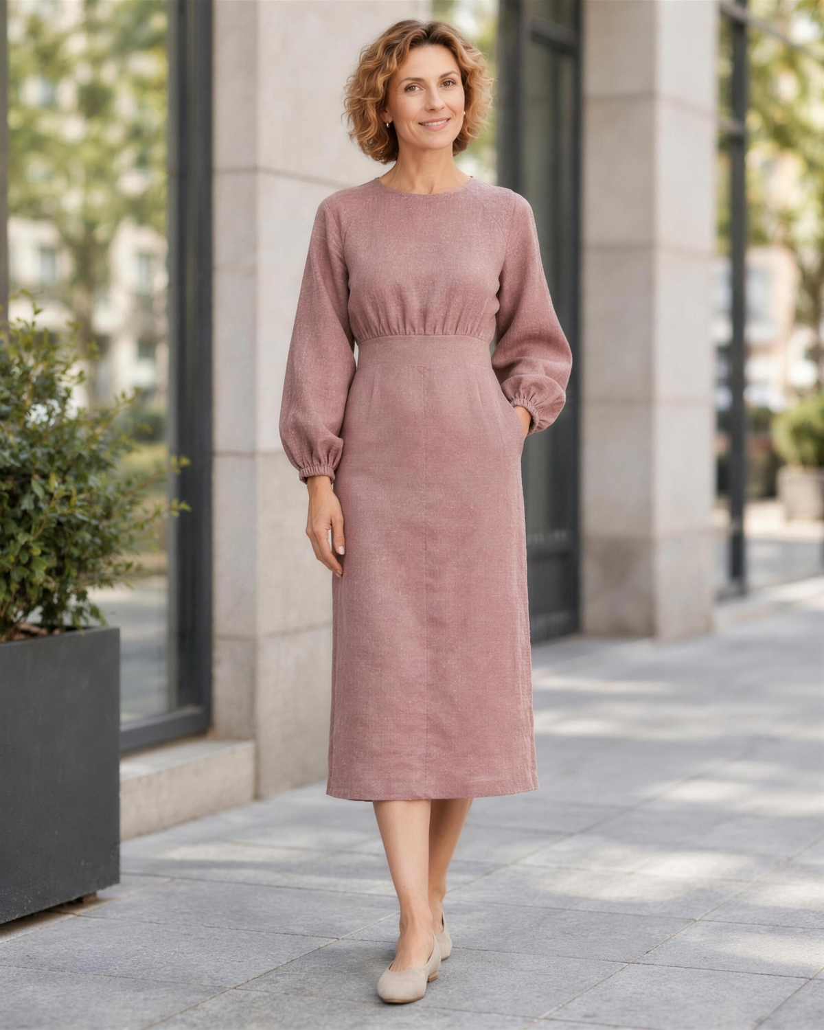 A woman standing on a city street, smiling, wearing a dusty rose linen midi dress with a gathered waist. #Color_Dusty rose