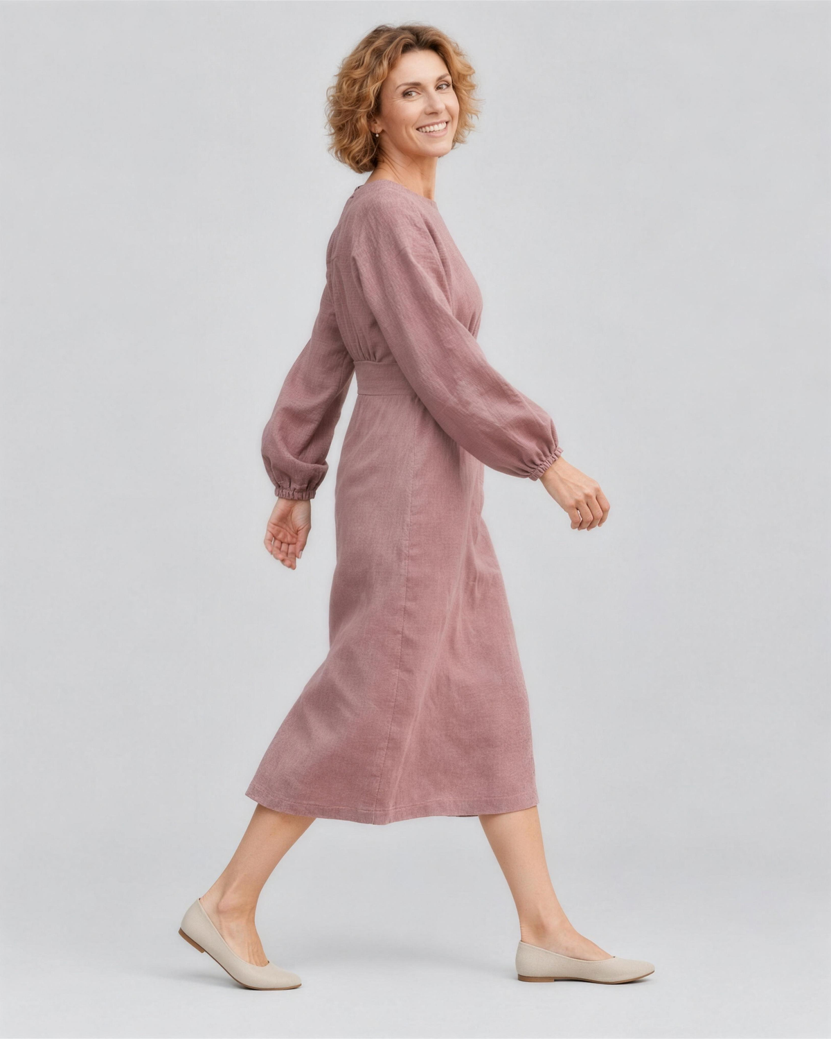 A woman walking, side view, wearing a dusty rose linen midi dress, showing how the linen fabric moves. #Color_Dusty rose