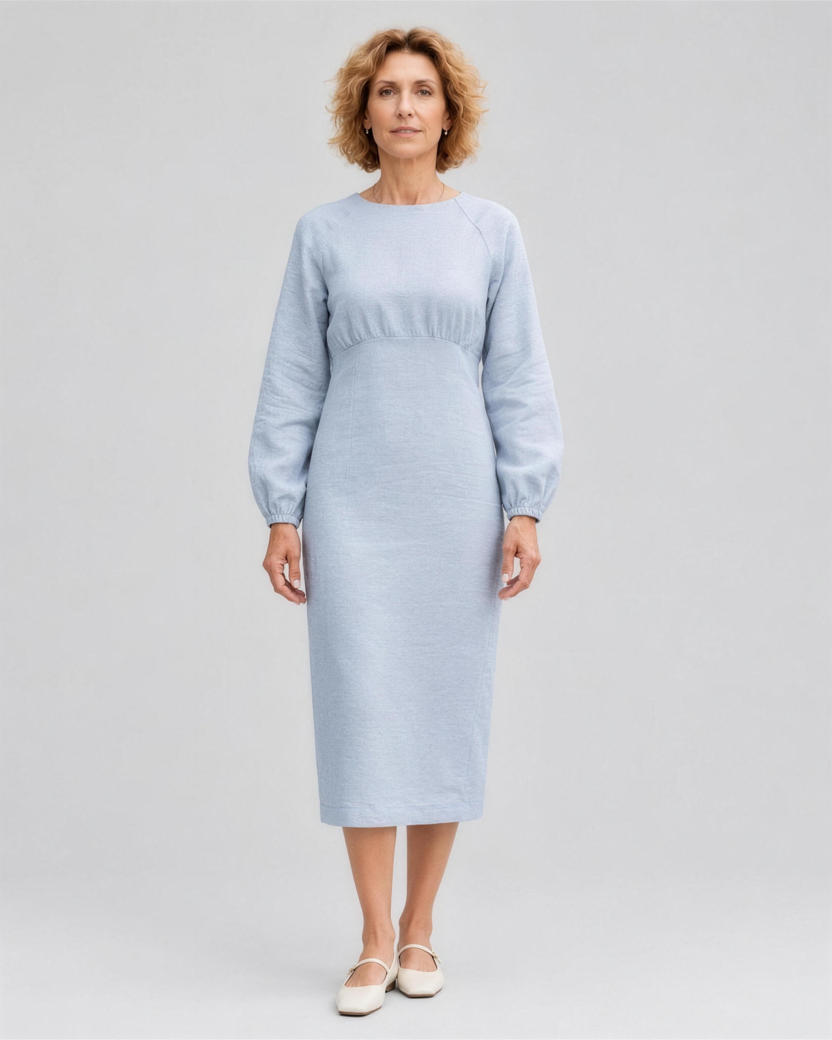 A woman standing in a studio, facing camera, full length, wearing a pale light blue linen midi dress with a gathered waist and elastic cuffs. #Color_Light blue