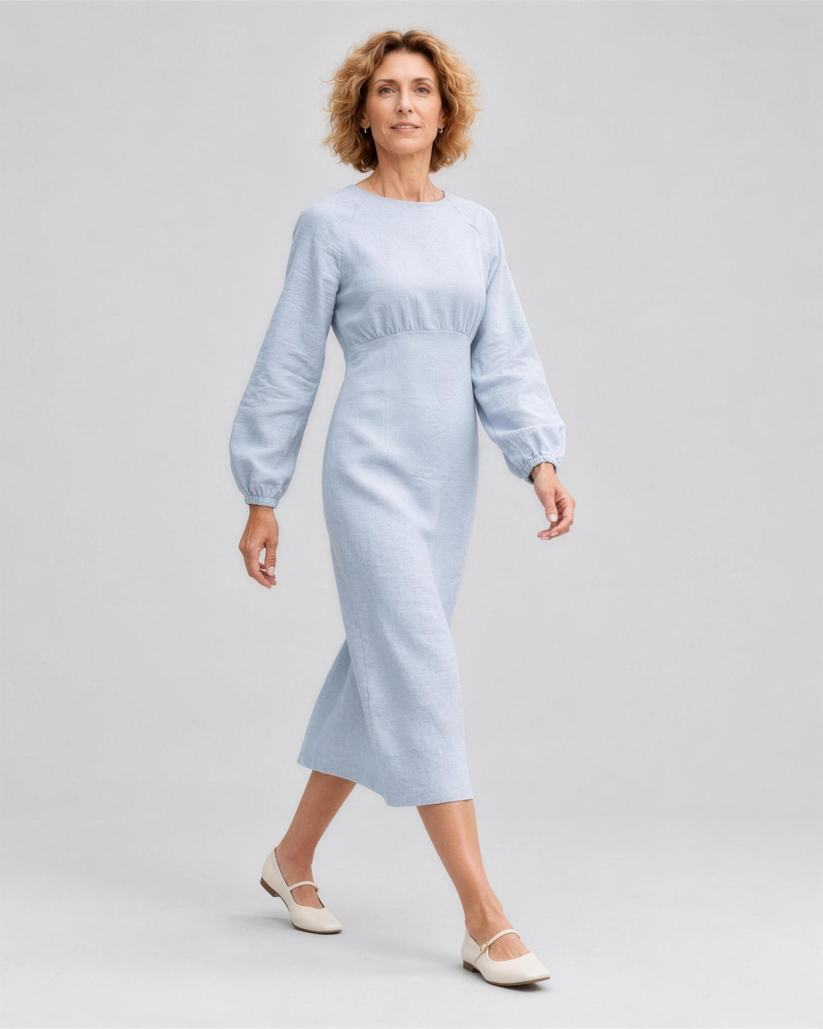 A woman walking, side view, wearing a pale light blue linen midi dress, showing how the linen fabric moves. #Color_Light blue