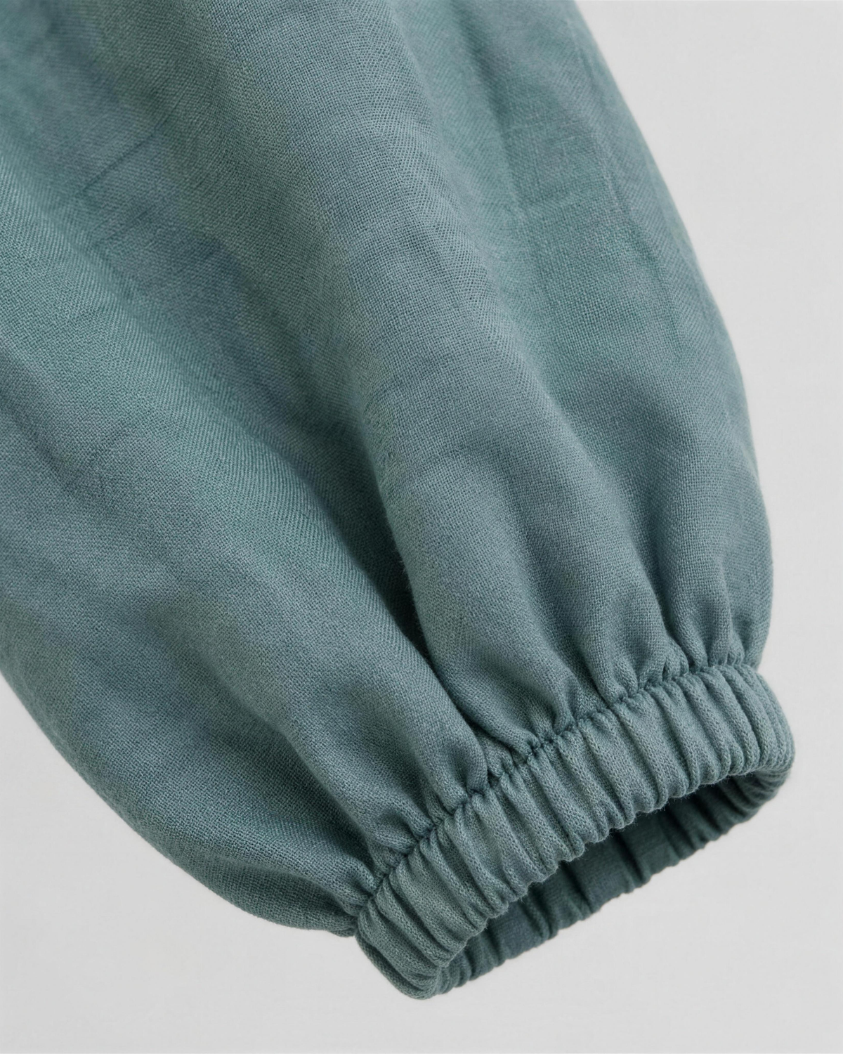 Close-up of muted dusty blue-green teal linen fabric texture and sleeve cuff detail on a midi dress. #Color_Teal