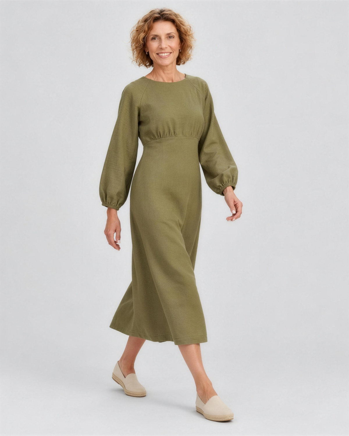 A woman walking, side view, wearing an olive green linen midi dress, showing how the linen fabric moves. #Color_Olive green