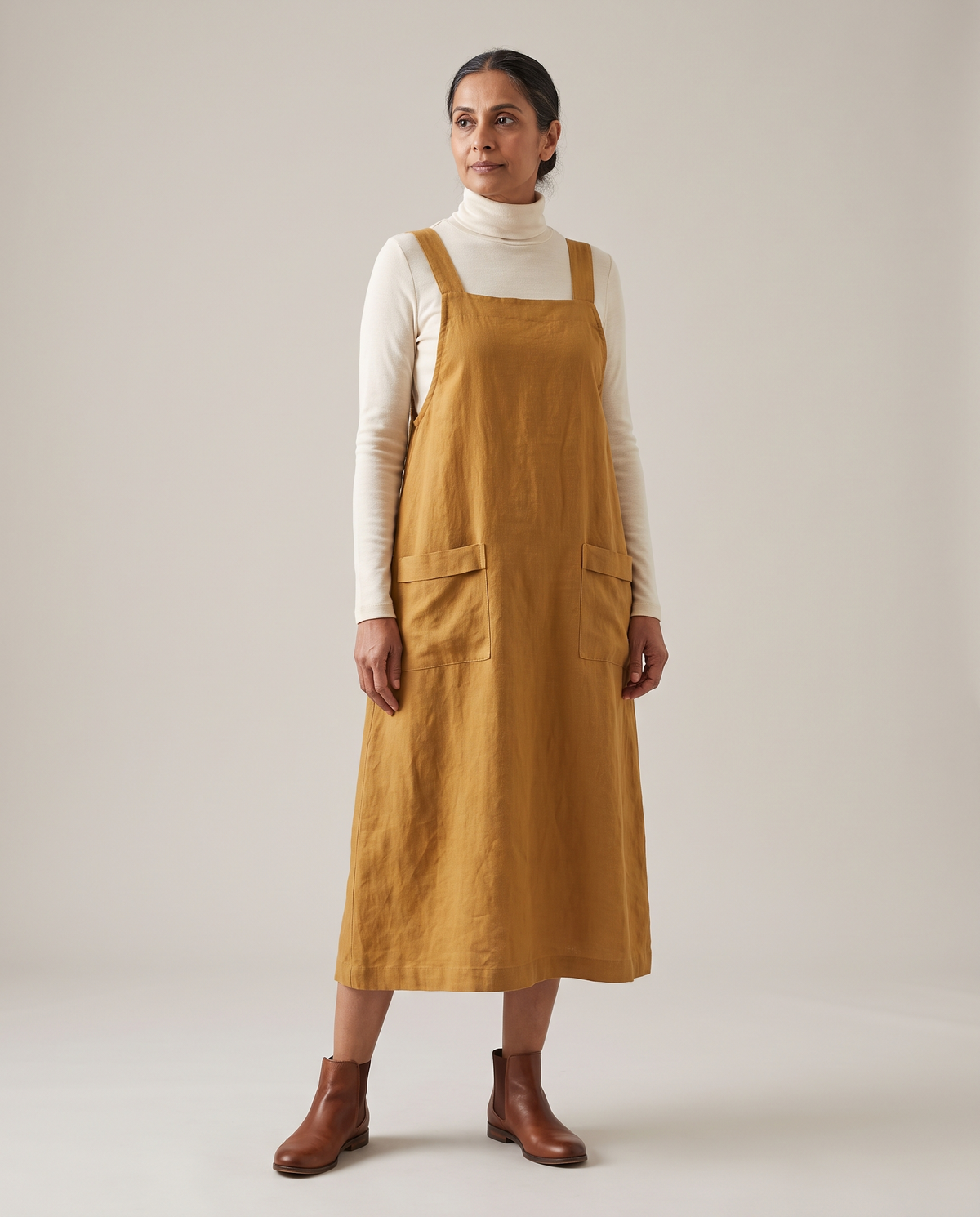 LAYER linen pinafore dress in Ochre over a cream turtleneck, front view