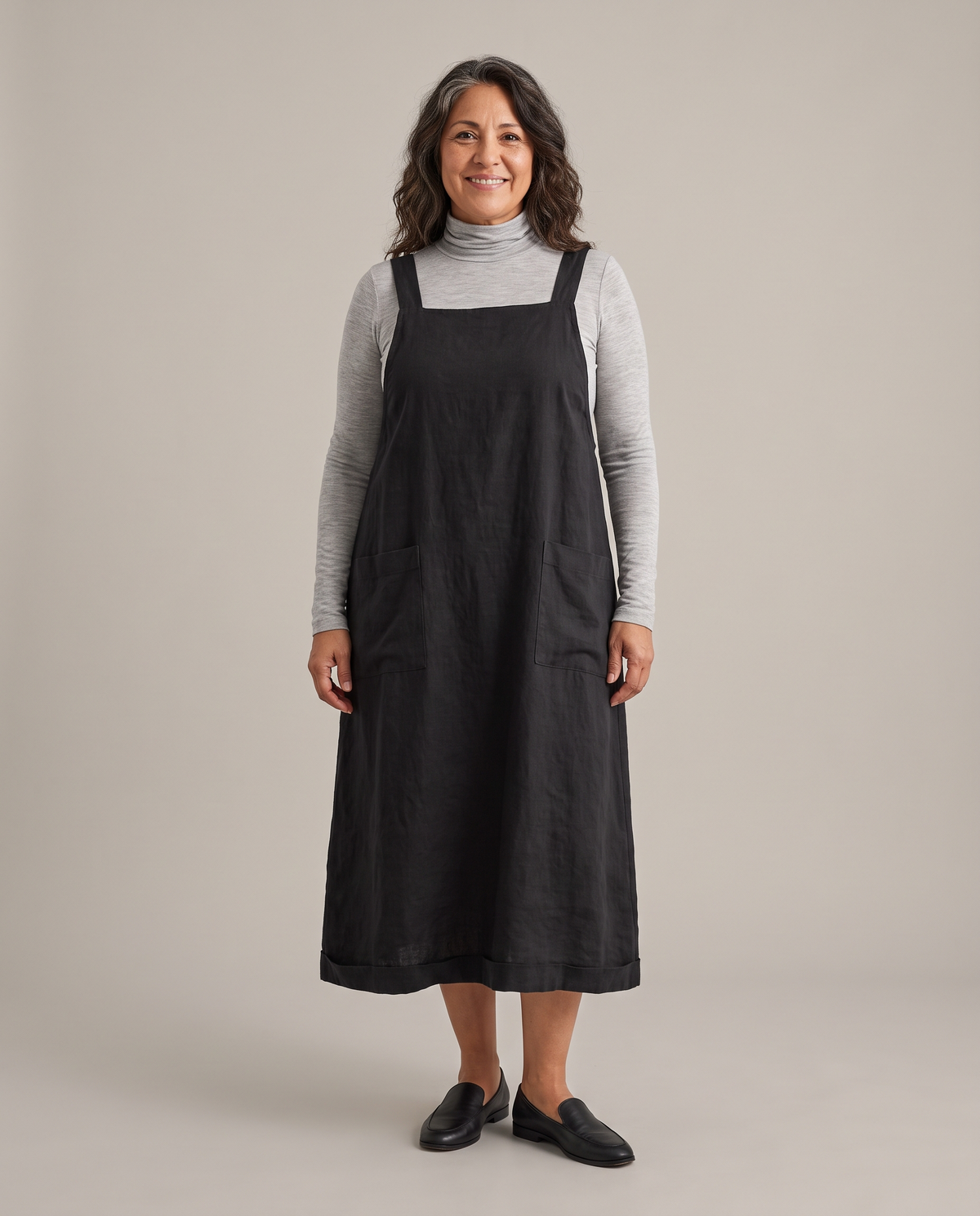 LAYER linen pinafore dress in Black over a grey turtleneck, front view