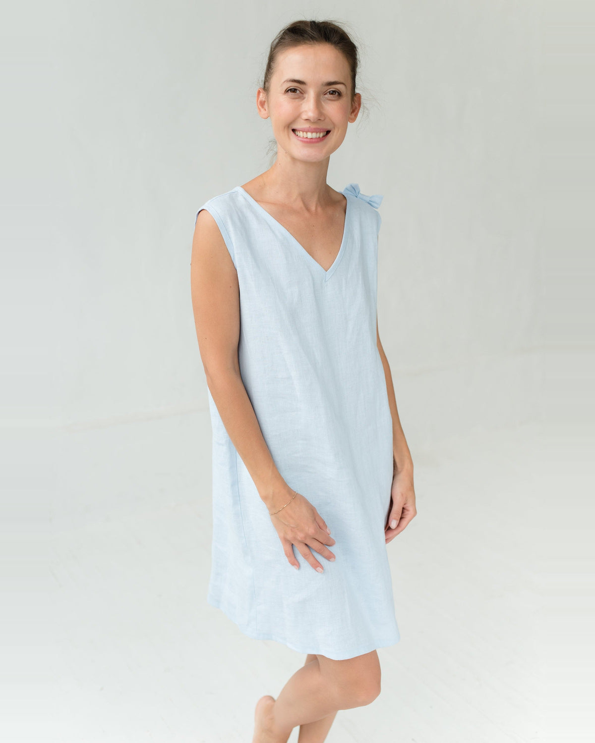 A woman in a light blue linen night dress with a wide plunging V neckline and a small bow on the shoulder.