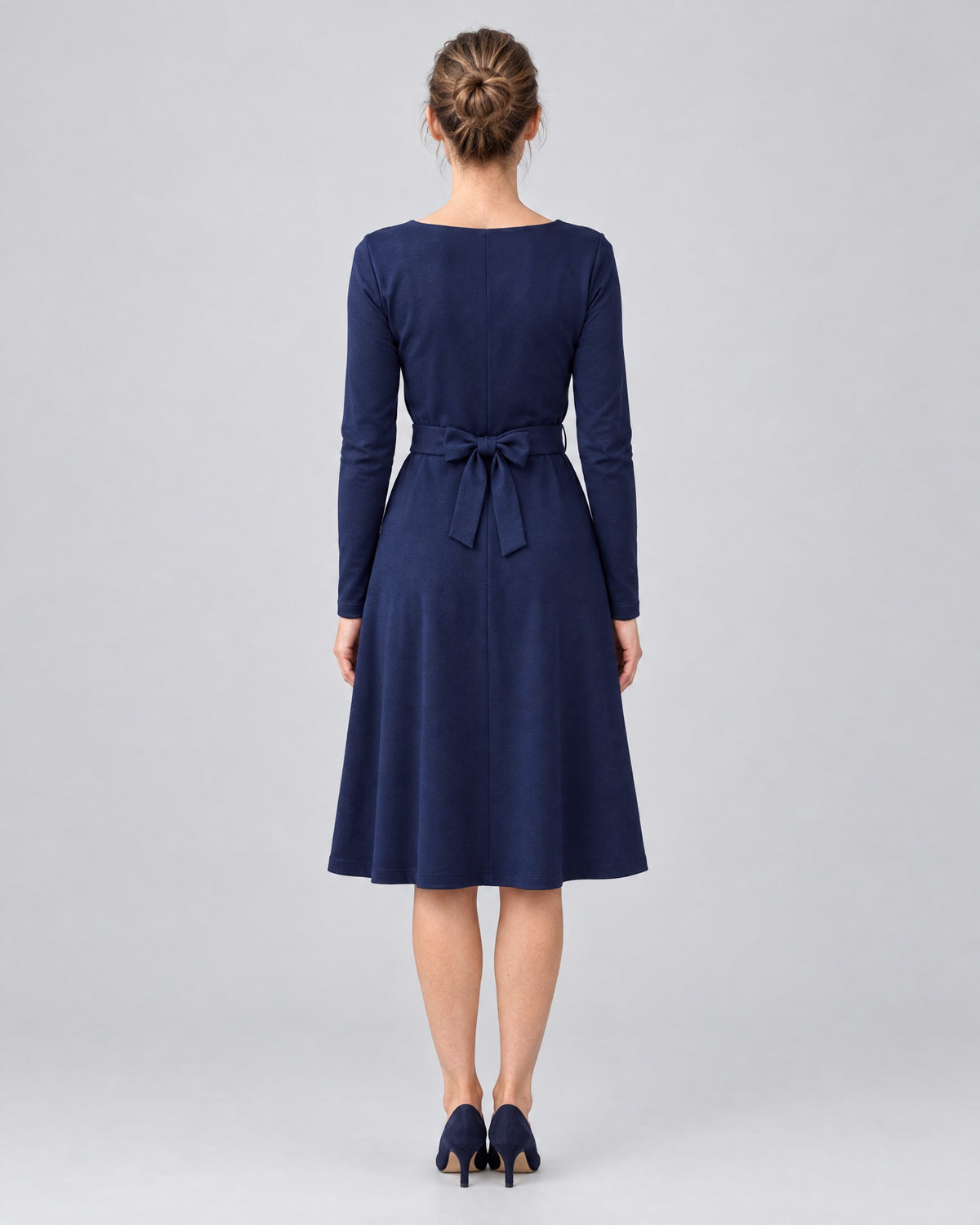 Frau in einem langärmeligen Punto-Milano-Kleid in Marineblau mit V-Ausschnitt und Gürtelschleife, Rückansicht, ganze Länge.