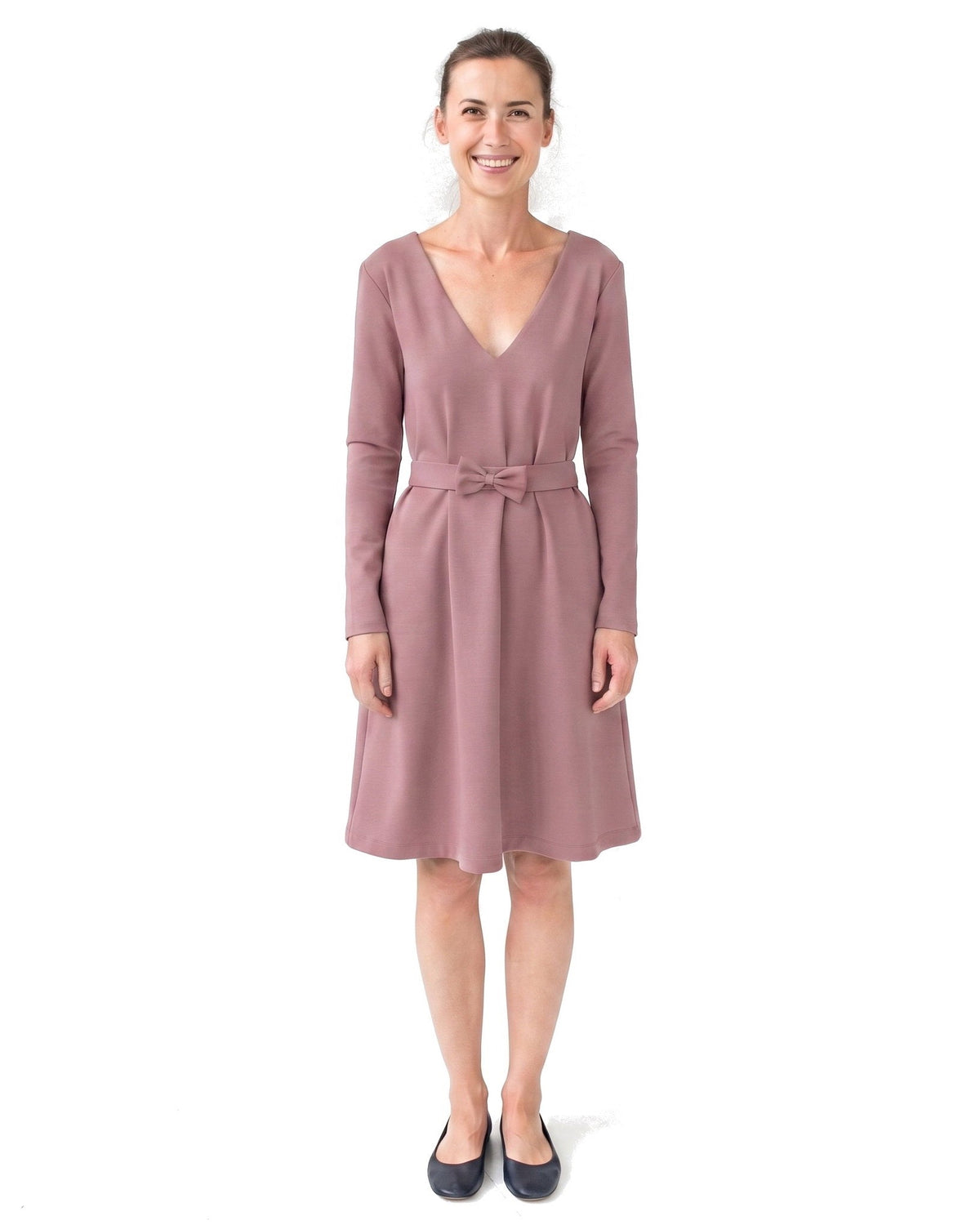 A woman modeling a dusty rose long-sleeve V-neck dress with a matching fabric tie belt, paired with black flats, against a plain white background. #Color_Dusty rose